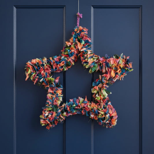 A star-shaped wreath made from colorful sari offcuts suspended against a blue door