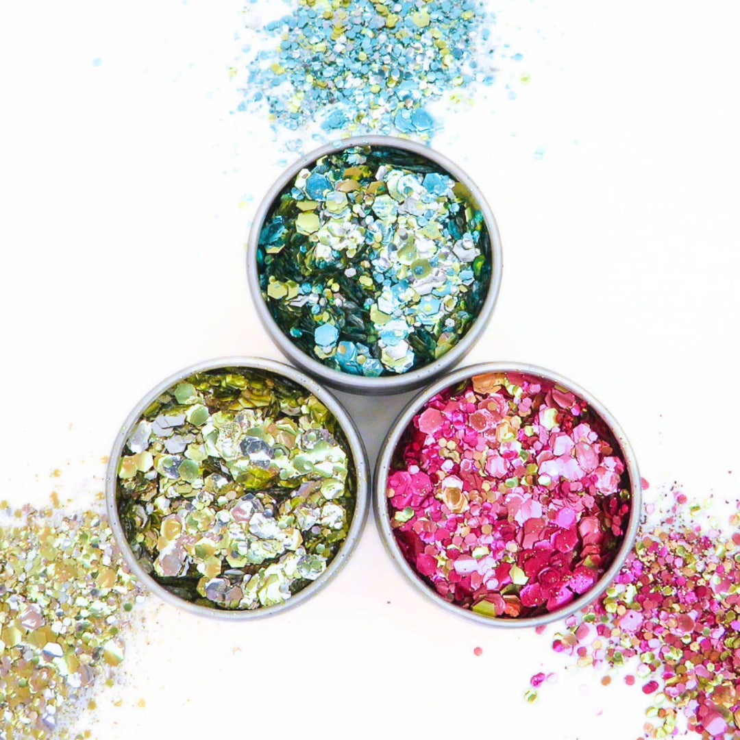 Three small containers filled with colorful glitter on a white background