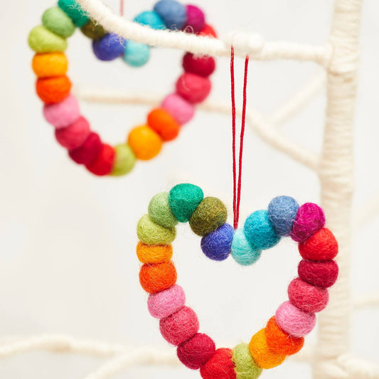 Colorful heart-shaped decorations made of felt balls hanging on a white background