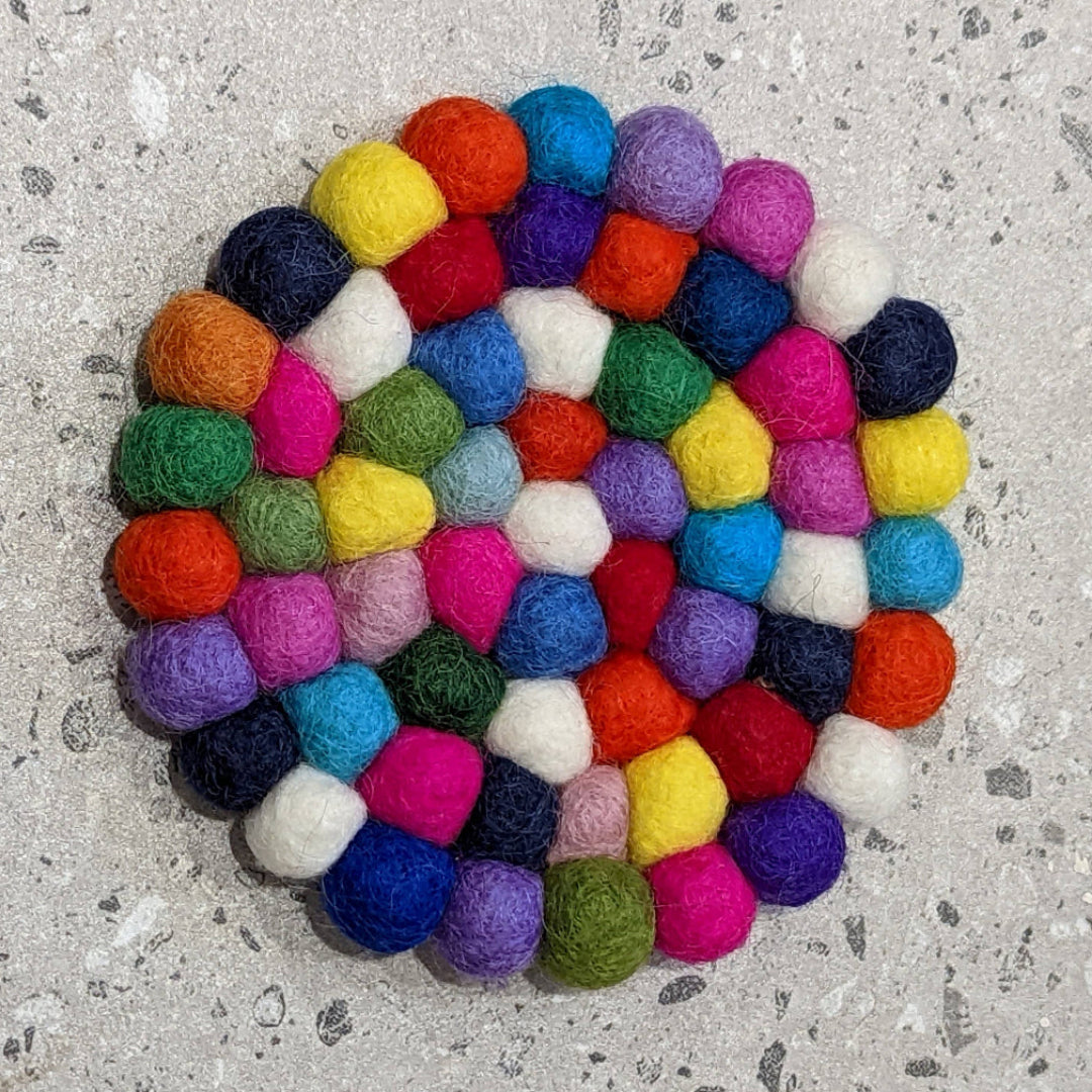Multicolored felt ball coaster on a gray surface