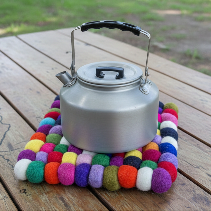 Silver kettle on a colorful felt trivet on a wooden surface