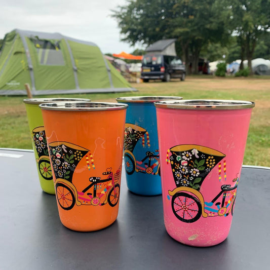 stainless steel enamelled wine tumblers with hand painted colourful rickshaw designs on a camping table with tents and trees in the background.
