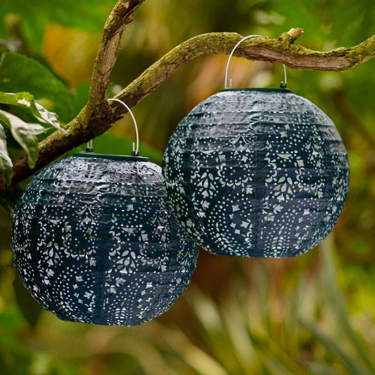 Two navy decorative solar lanterns with metal hooks hanging from a branch