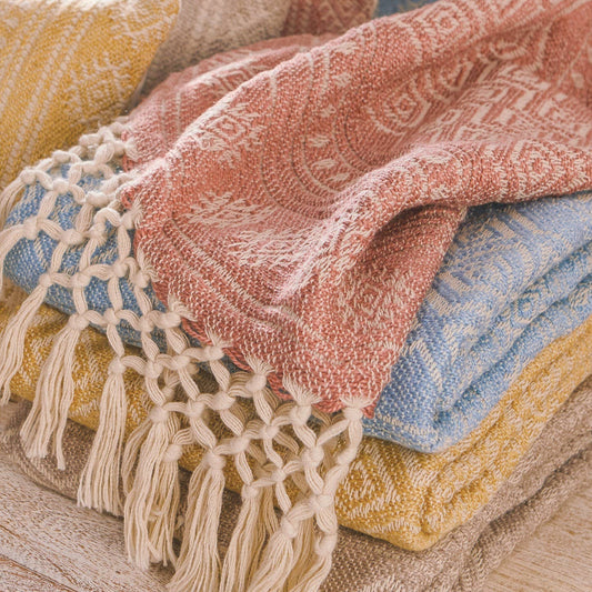 Stack of cosy and colourful textured throws with tassels in light red, blue, gold and grey