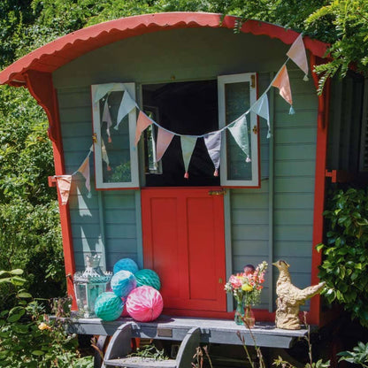 Colorful shepherd's hut in a garden with decorative items and pastel bunting.