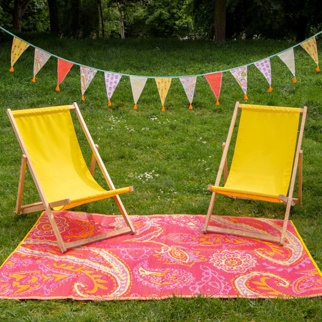 Two yellow deck chairs on a pink paisley rug with a colorful paisley bunting string across the top.