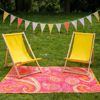 Two yellow deck chairs on a pink paisley rug with a colorful paisley bunting string across the top.