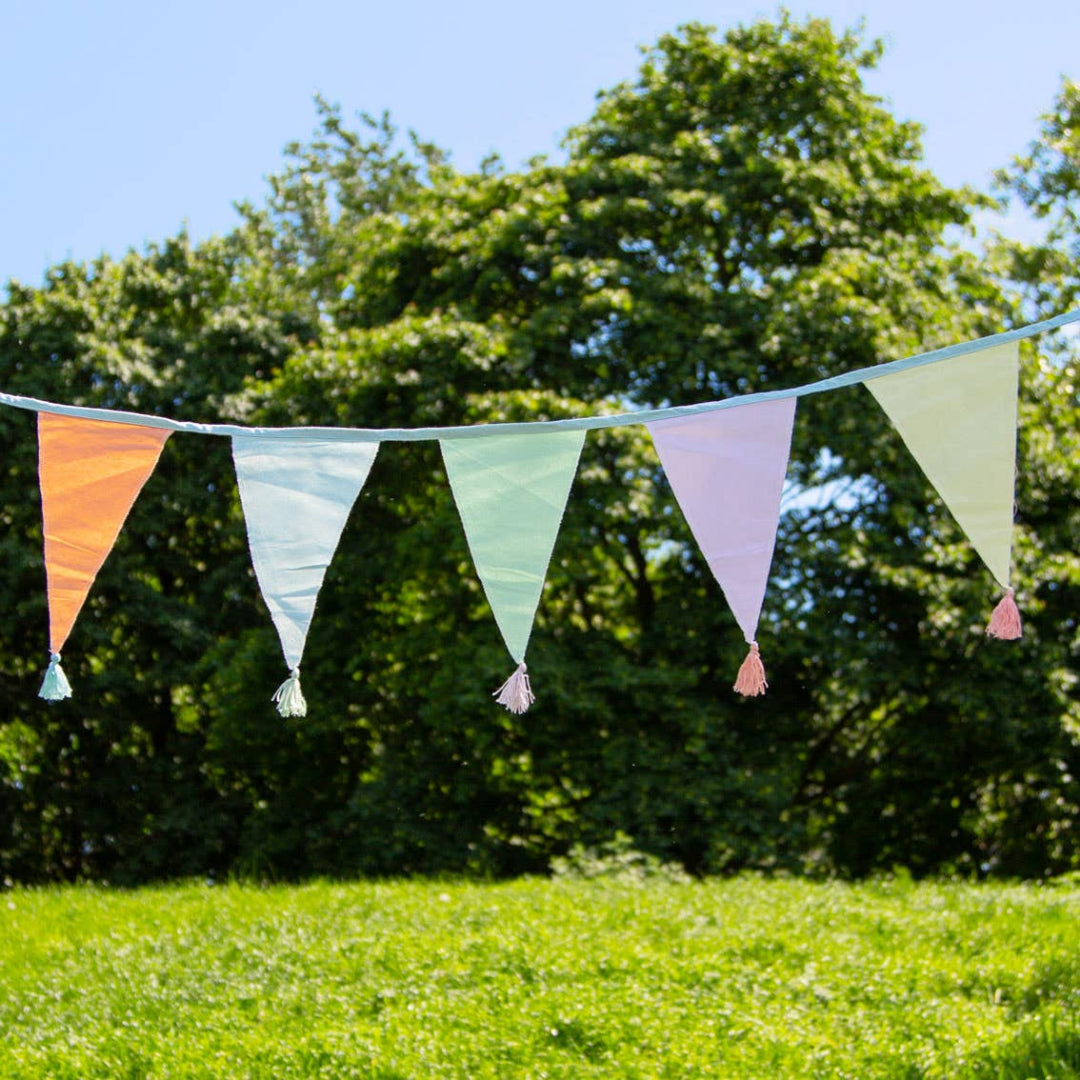Pastel bunting flags hanging outdoors against a green tree background