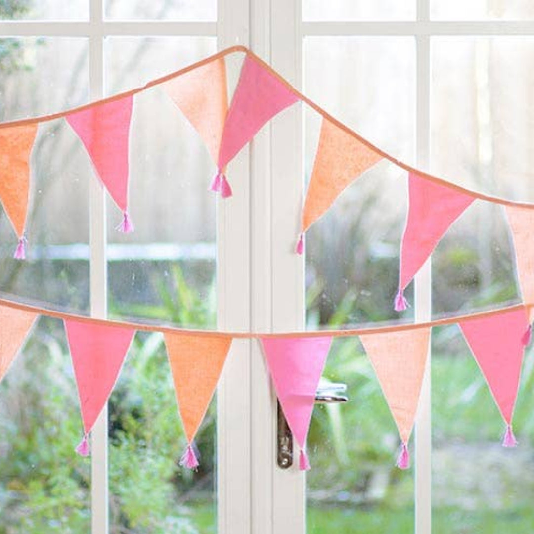 Colorful pink bunting flag garland hanging on a white door with a garden view.
