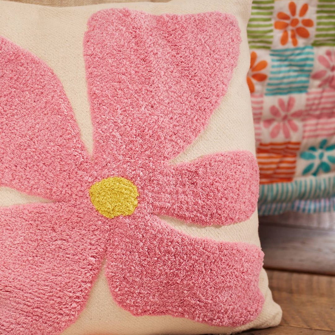 Decorative pillow with a pink flower design against a colourful bedspread
