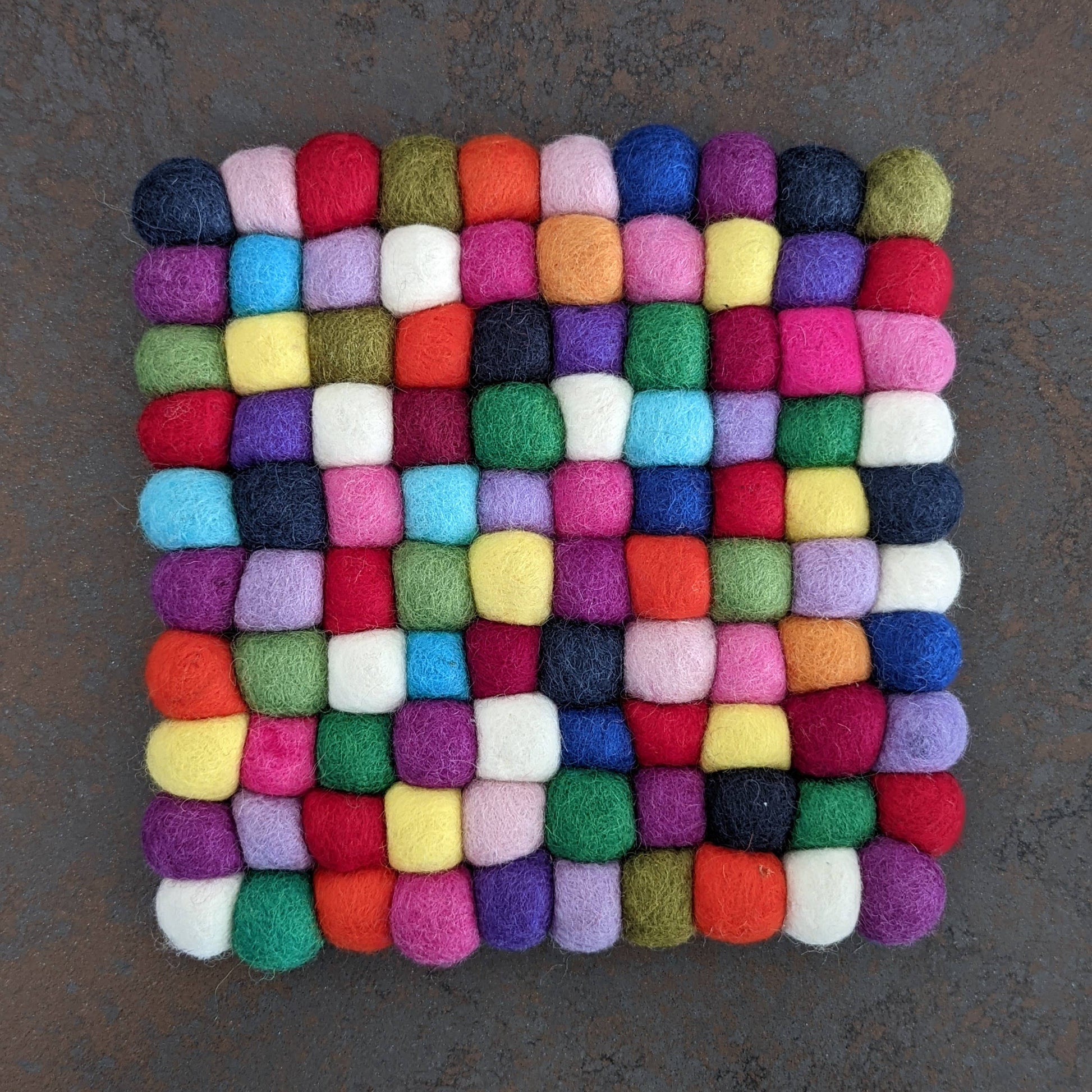 Multicolored pompom trivet square on a dark background