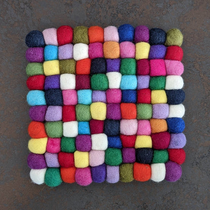 Multicolored pompom trivet square on a dark background
