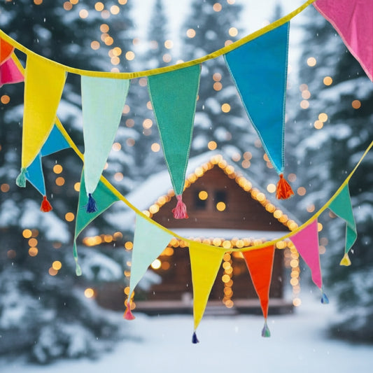 rainbow coloured bunting draped between trees on a woodland campsite.