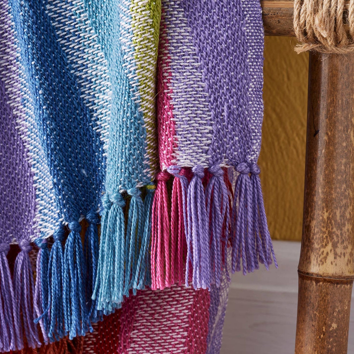 rainbow throw with tassels draped over a wooden surface.