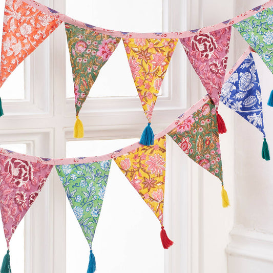 Colorful fabric bunting with tassels hanging against a white window frame.