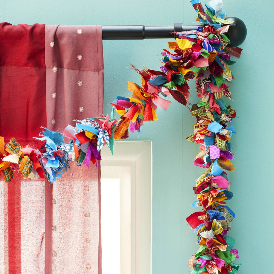 Colorful fabric garland hanging on a curtain rod against a light blue wall.