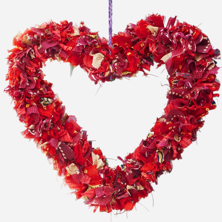 Heart-shaped wreath made of red recycled sari fabric on a light blue wall 