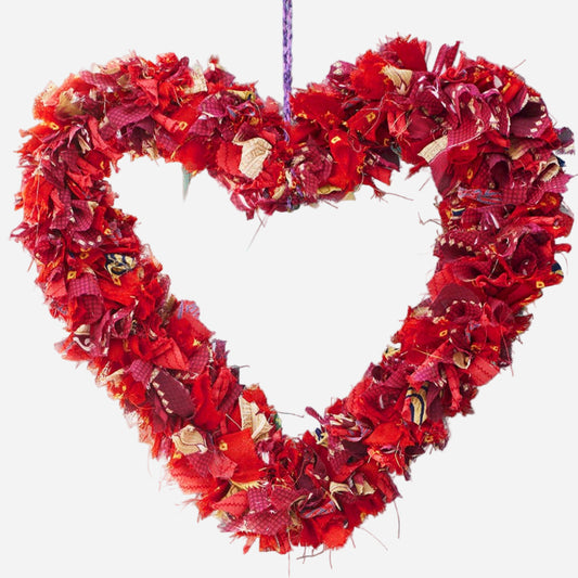 Heart-shaped wreath made of red recycled sari fabric on a light blue wall 