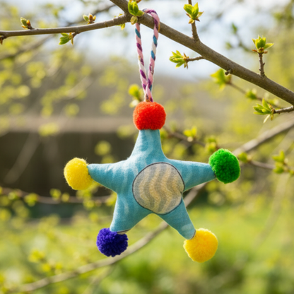 Colorful star-shaped decoration hanging from a tree branch with a blurred natural background