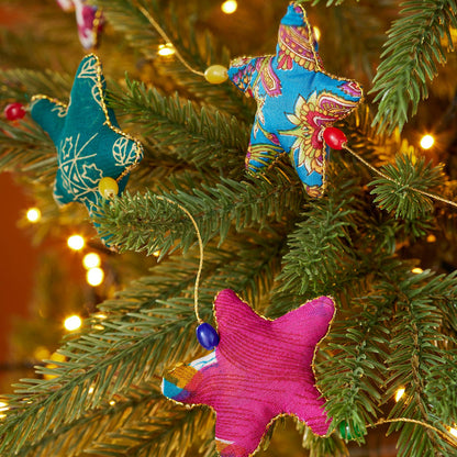 Colorful star fabric Christmas garland hanging on a green Christmas tree with gold strings and colourful beads connecting them.