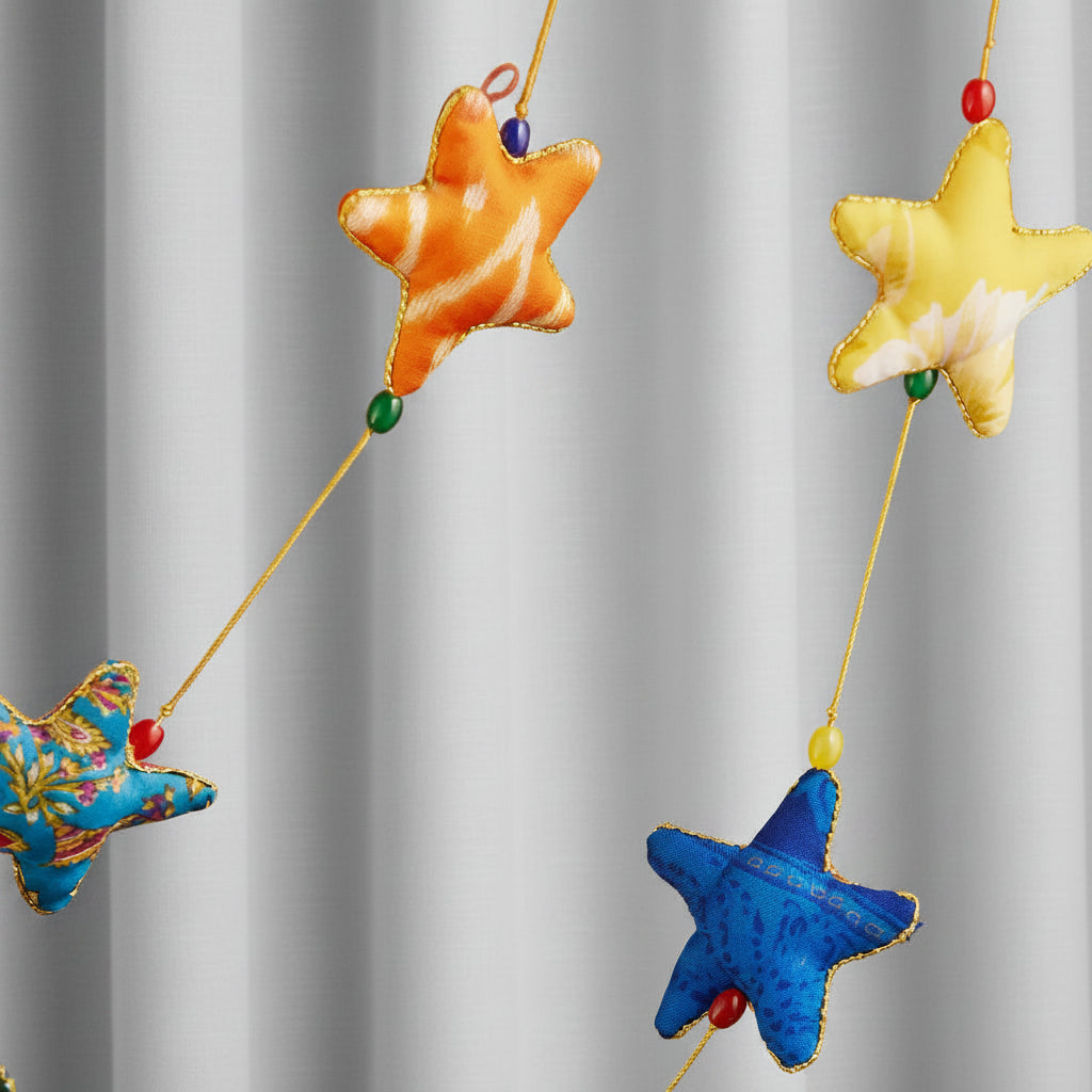 Colorful fabric star garland hanging against a warm brown wooden door. The stars are in orange, yellow, blue, pink, and a multicolor floral pattern, strung on thin yellow cords with small beads.