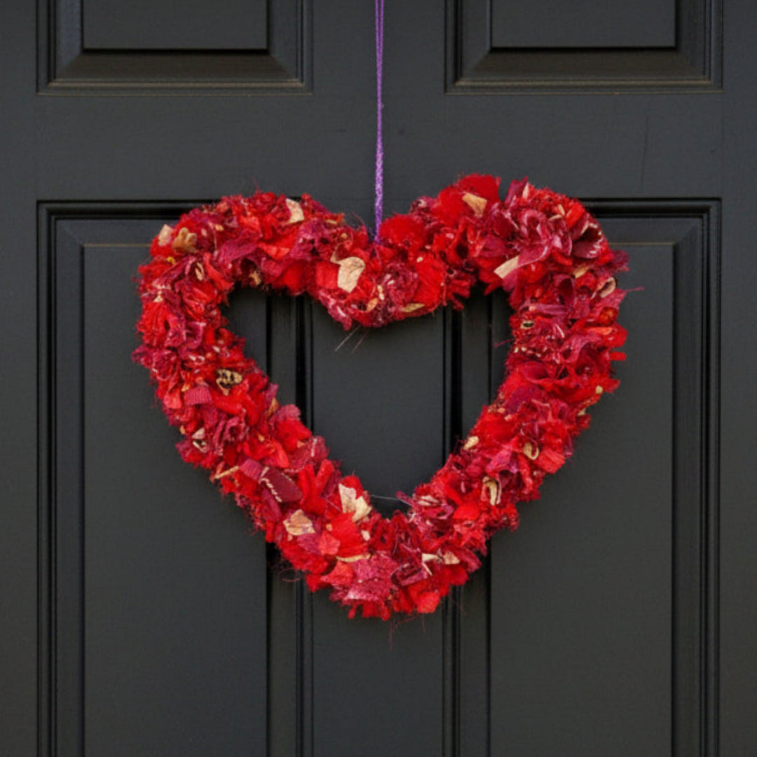 Heart-shaped red wreath hanging on a purple string against a black front door. 