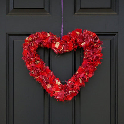 Heart-shaped red wreath hanging on a purple string against a black front door. 