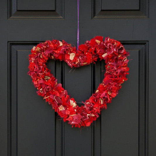 Heart-shaped red wreath hanging on a purple string against a black front door. 