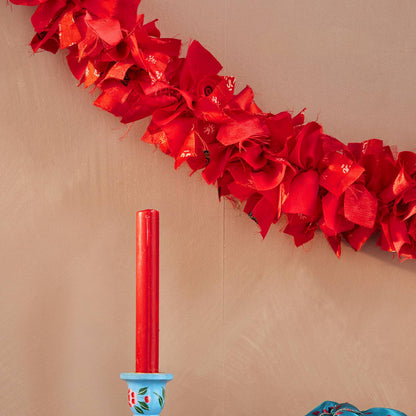 red fabric garland or tinsel on a beige wall background with a red candle