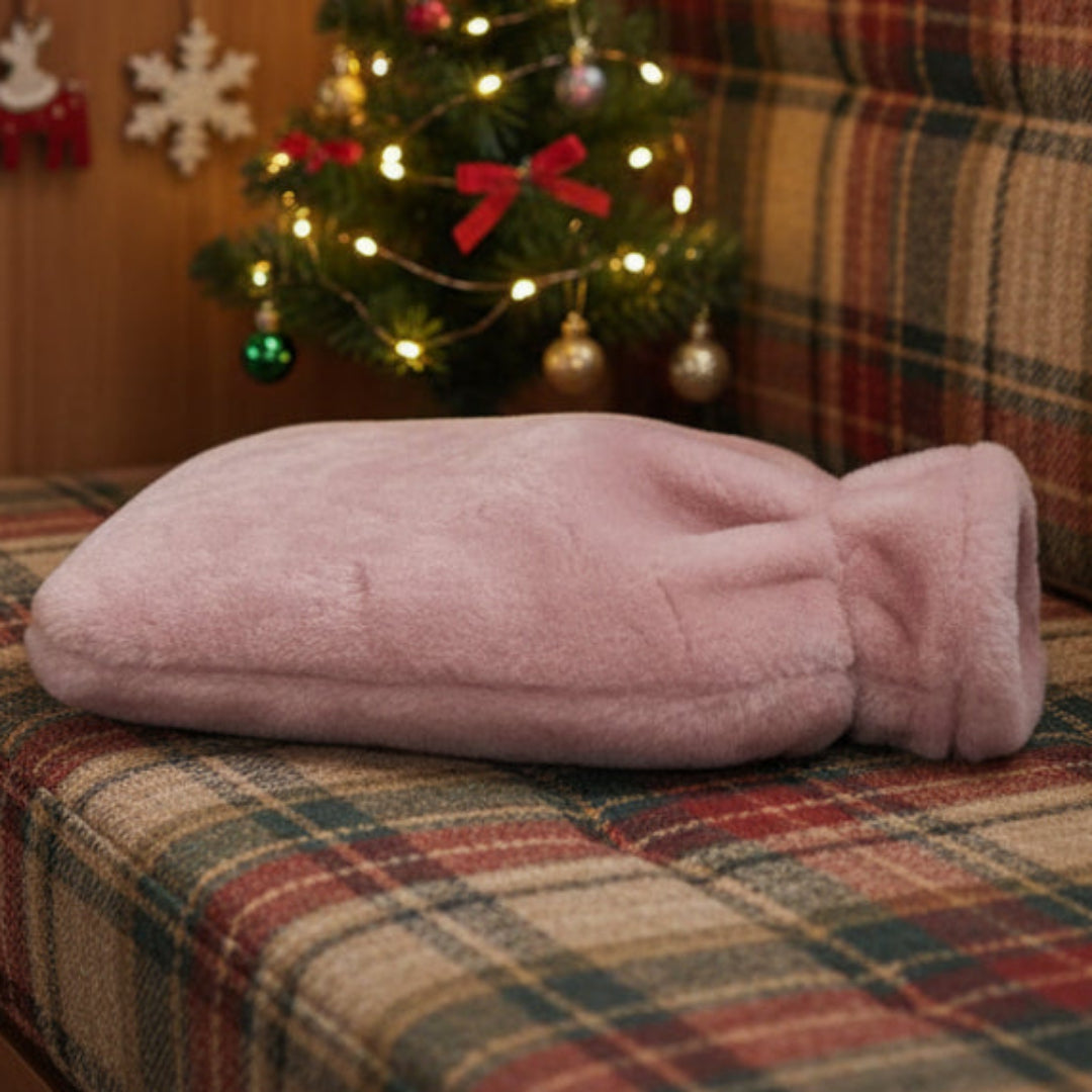 Rose pink sheepskin hot water bottle on a plaid caravan bench with a decorated Christmas tree in the background