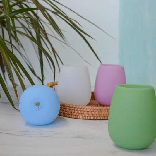 Set of four colourful, silicone wine tumblers (pastel green, blue, pink and white) on a light surface with a plant in the background