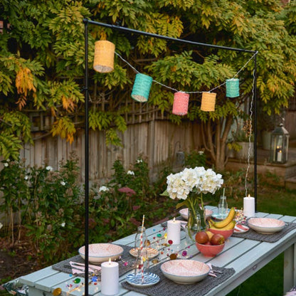 Outdoor dining setup with a table, chairs, and decorative multicolour lanterns in a garden.