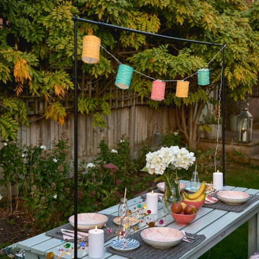 Outdoor dining setup with a table, chairs, and decorative multicolour lanterns in a garden.