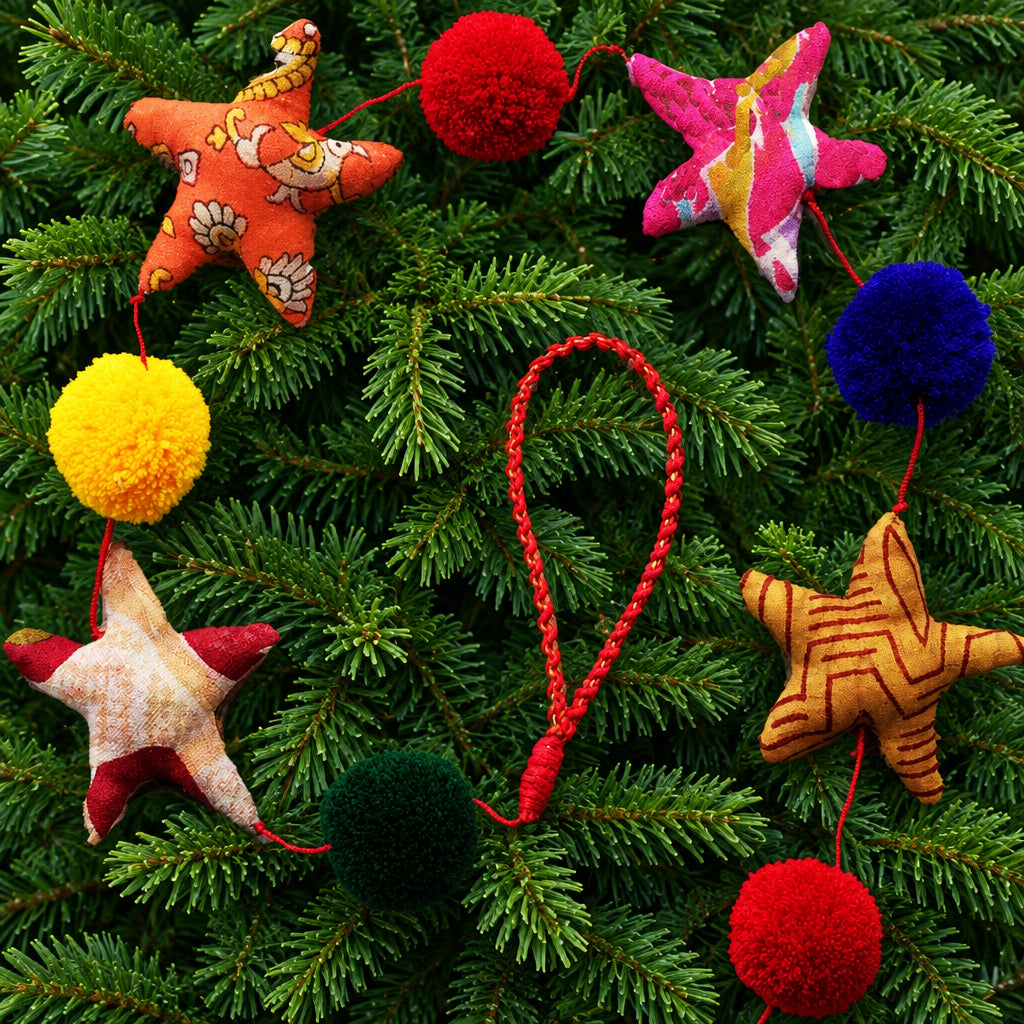 A colorful fabric star and pom-pom garland with red string displayed on a clean green pine background