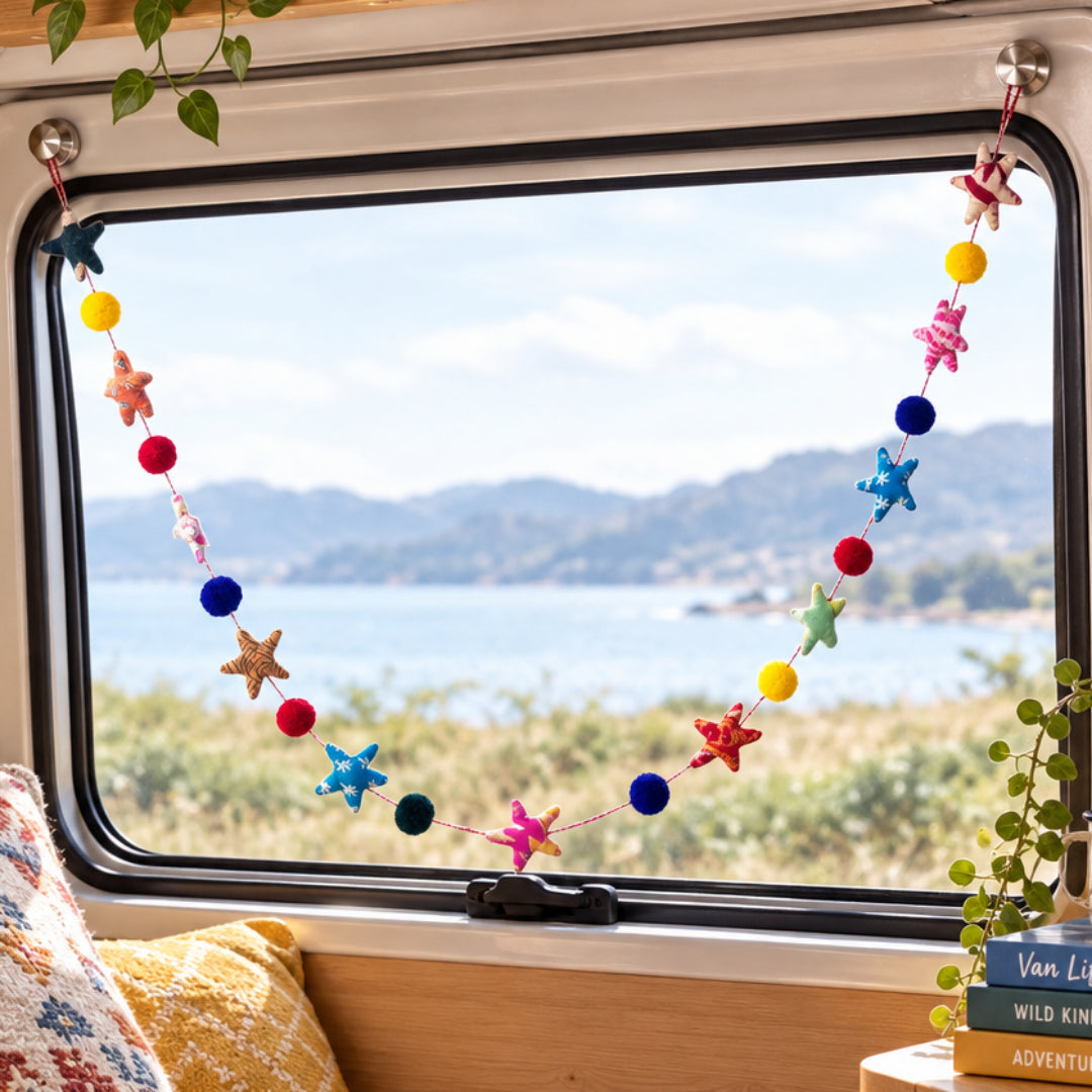 A colorful star and pompom garland hanging across  a  campervan window