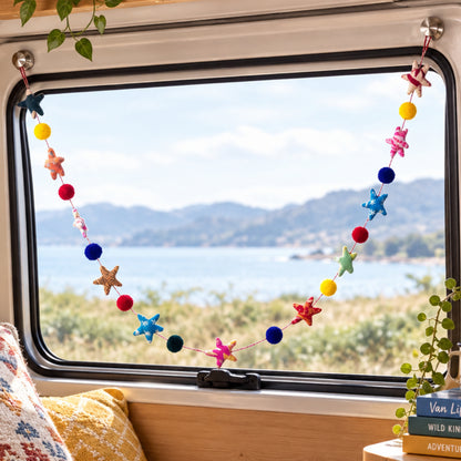 A colorful star and pompom garland hanging across  a  campervan window