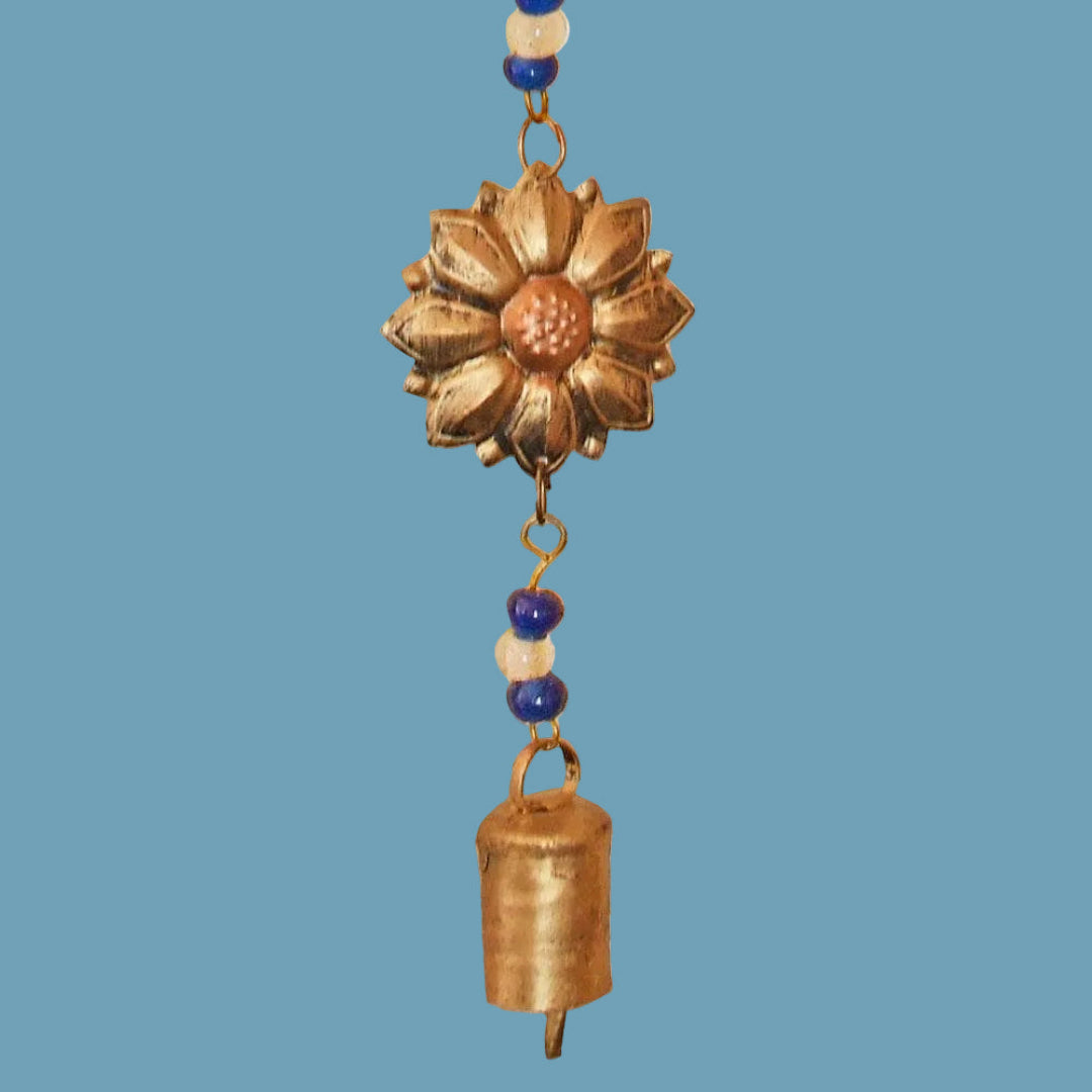 Decorative hanging wind chime with a sunflower design and bell on a blue background