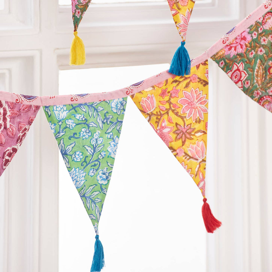 Colorful floral patterned bunting with tassels against a white window frame.