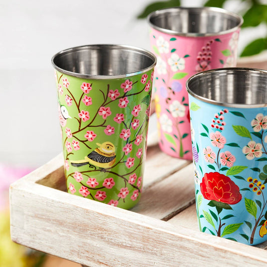 three beautiful hand painted enamel tumblers with stainless steel interior and lip, show on a small wooden tray.