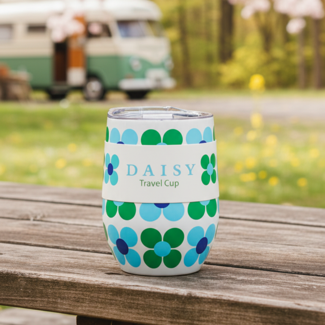 Floral-patterned travel cup with 'DAISY' branding on a wooden surface outdoors.