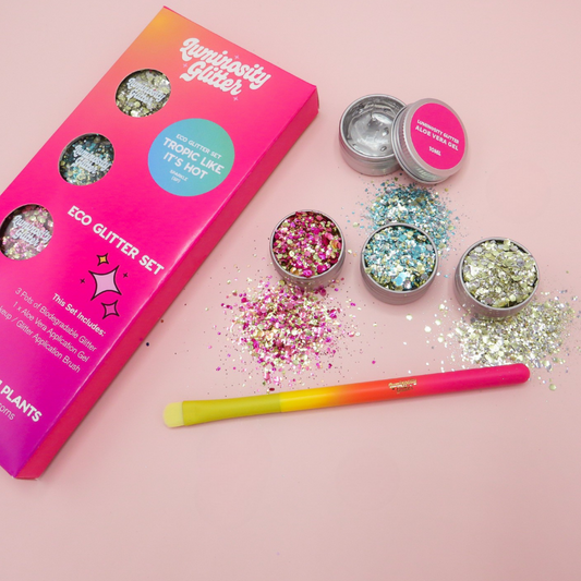 Luminosity Glitter eco glitter set with open containers and a glitter brush on a pink background
