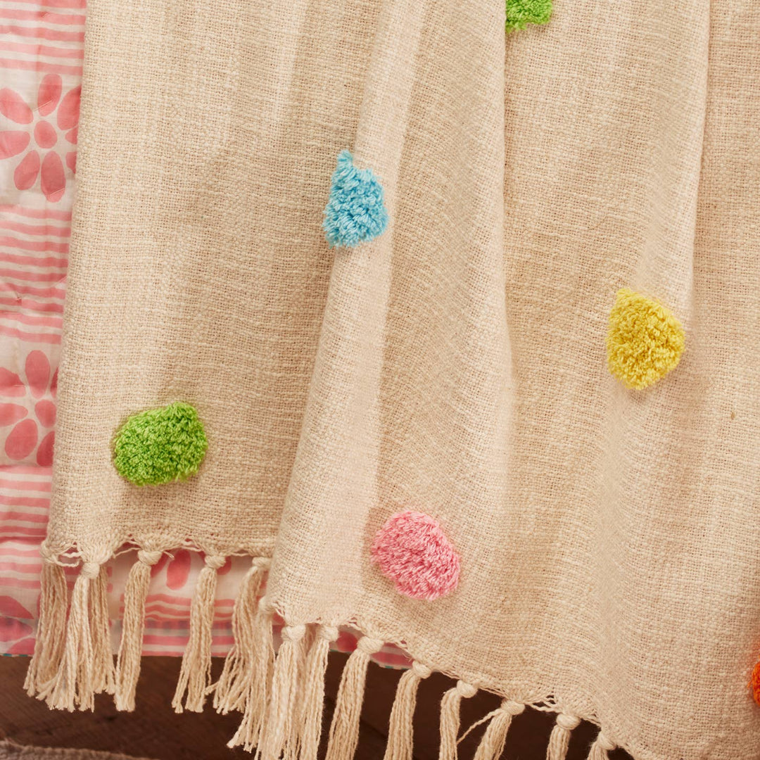 Close up of natural throw with colorful tuft dots on a floral drape.