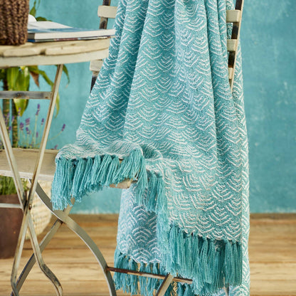 Turquoise textured throw blanket with tassels draped over a chair against a blue wall.