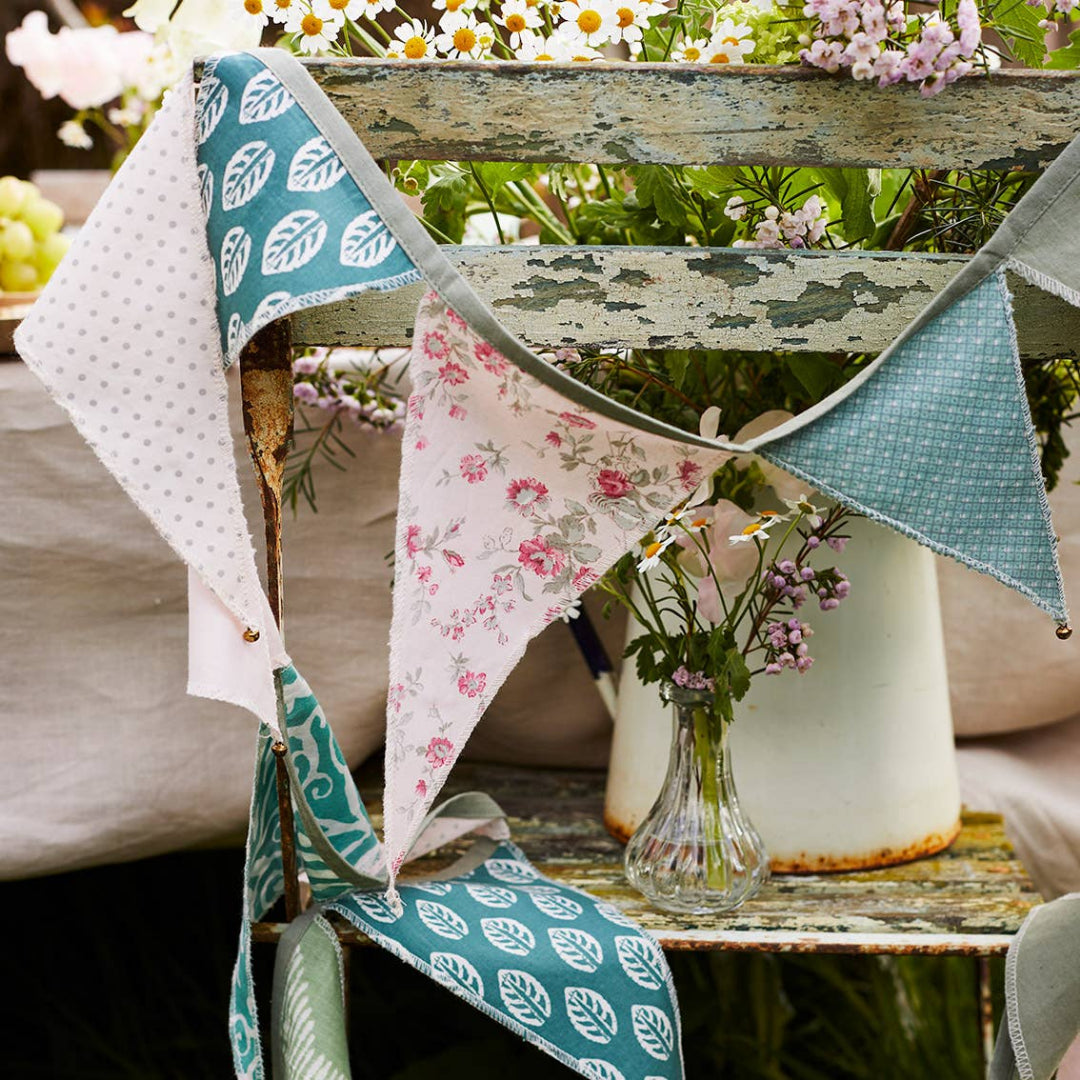 Decorative fabric bunting with floral and leaf patterns on a wooden bench outdoors.