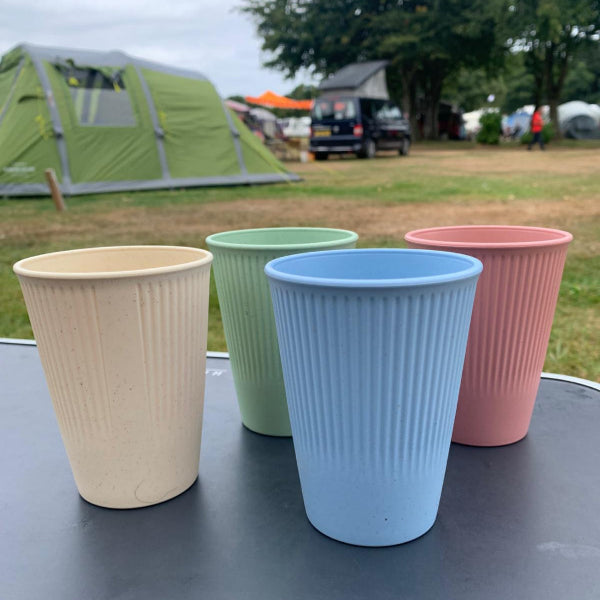 Four colorful camping cups on a table with a camping scene in the background