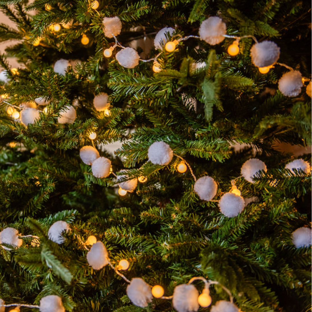 Decorated Christmas tree with lights and pom-pom ornaments in a room setting.
