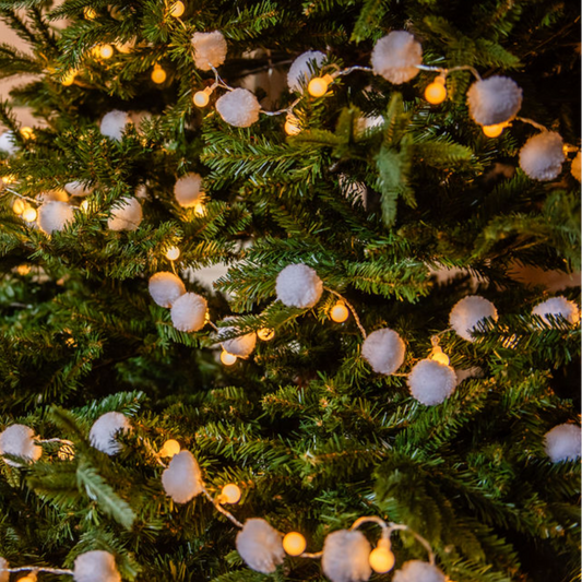 Decorated Christmas tree with lights and pom-pom ornaments in a room setting.