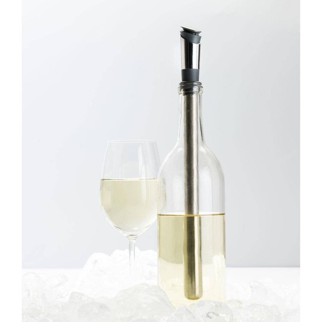 Clear wine bottle with cihll stick and wine pourer and a glass of white wine on a light gray background