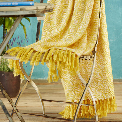 A bright yellow woven throw blanket with a geometric pattern and long fringe, draped over a folding chair in an outdoor patio setting.